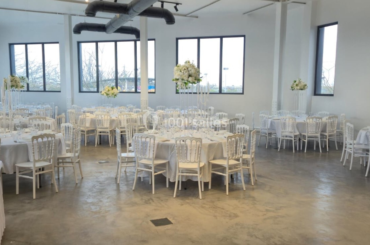 Salle de réception lumineuse avec des tables rondes décorées de nappes blanches et de fleurs élégantes.
