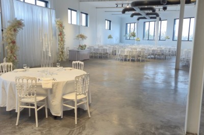 Miniature Location salle Épinay-sur-Seine (Seine-Saint-Denis) - Salle Delena #13 Salle lumineuse avec table ronde dressée, chaises blanches et centre de table floral sous de grandes fenêtres.