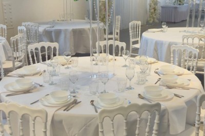 Miniature Location salle Épinay-sur-Seine (Seine-Saint-Denis) - Salle Delena #14 Salle lumineuse avec table ronde dressée, chaises blanches et centre de table floral sous de grandes fenêtres.