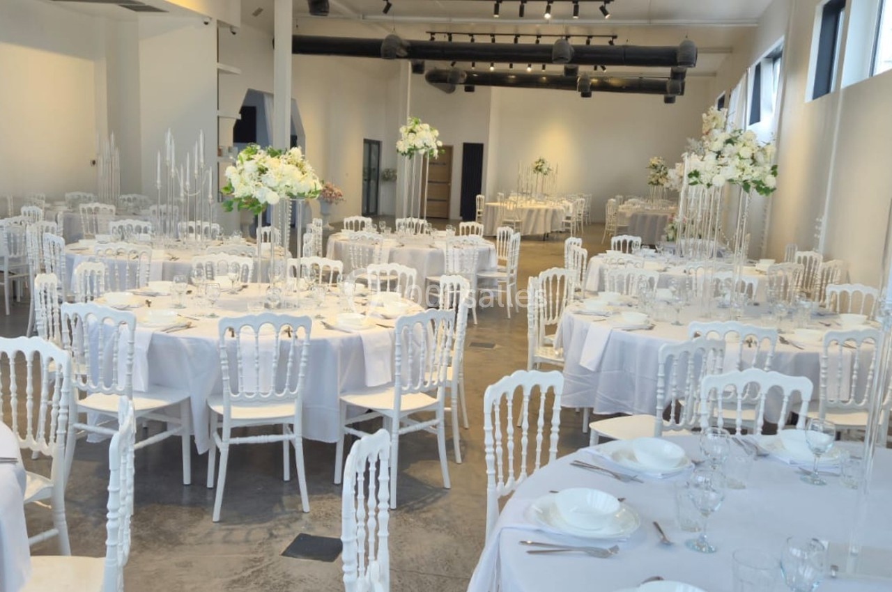Salle de réception élégamment décorée avec des tables rondes, nappes blanches et arrangements floraux.