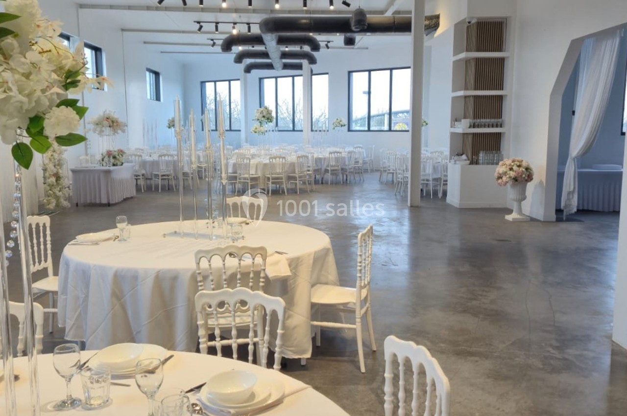 Salle de réception lumineuse avec tables rondes décorées de fleurs blanches et chaises blanches élégantes.