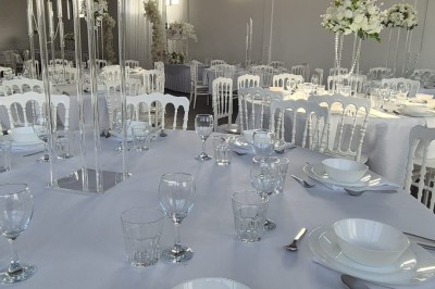 Miniature Location salle Épinay-sur-Seine (Seine-Saint-Denis) - Salle Delena #2 Salle lumineuse avec table ronde dressée, chaises blanches et centre de table floral sous de grandes fenêtres.