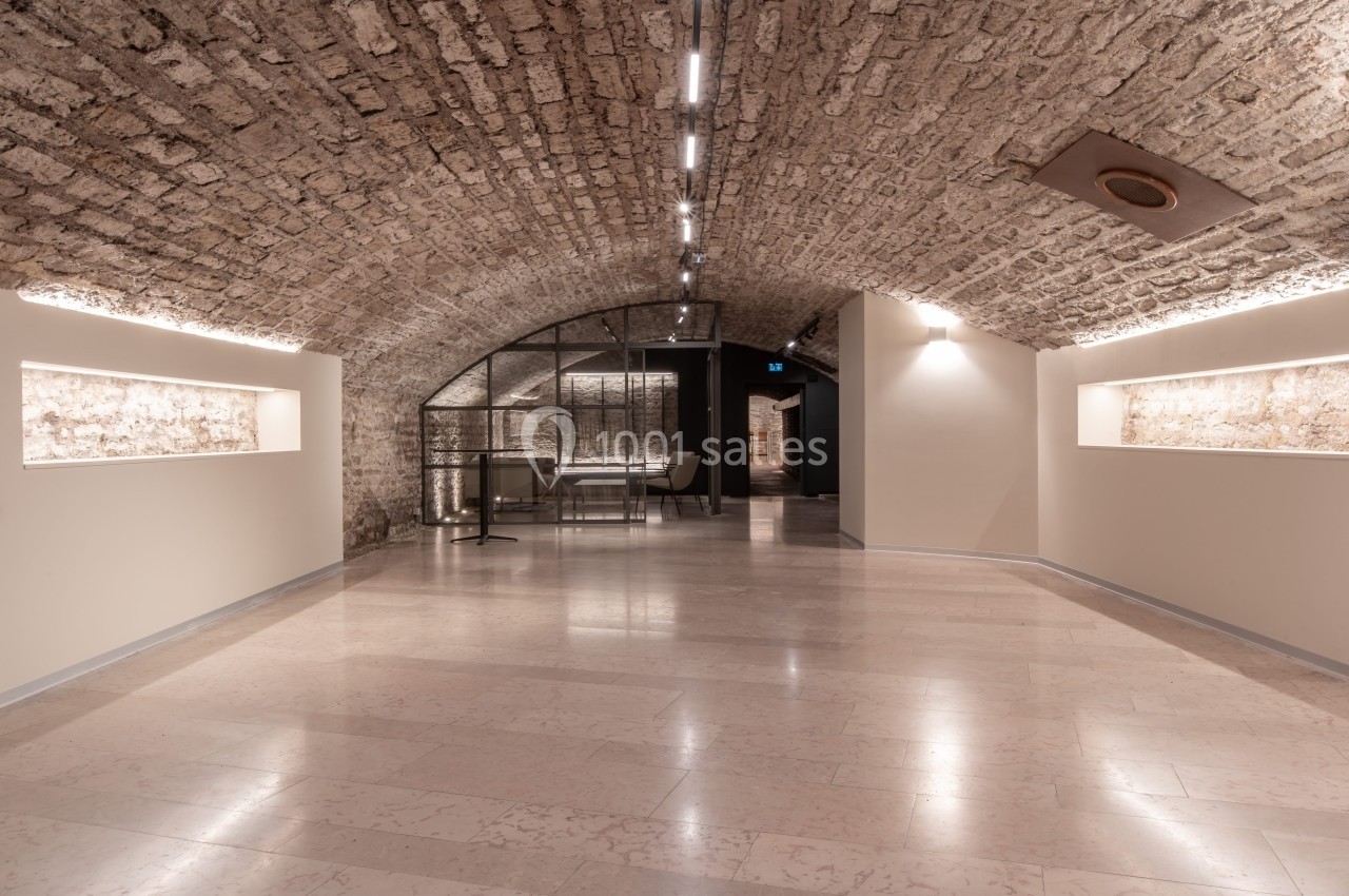 Salle voûtée en pierre avec éclairage intégré, sol en marbre clair et mobilier moderne en arrière-plan.