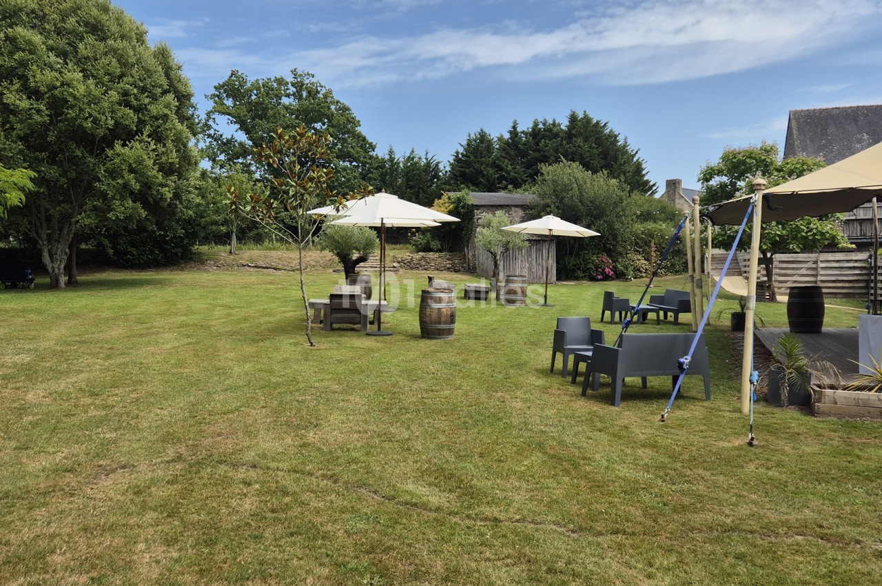 Vaste pelouse arborée avec mobilier de jardin en résine grise, parasols crème et tonneaux en bois, sous un ciel dégagé en extérieur.