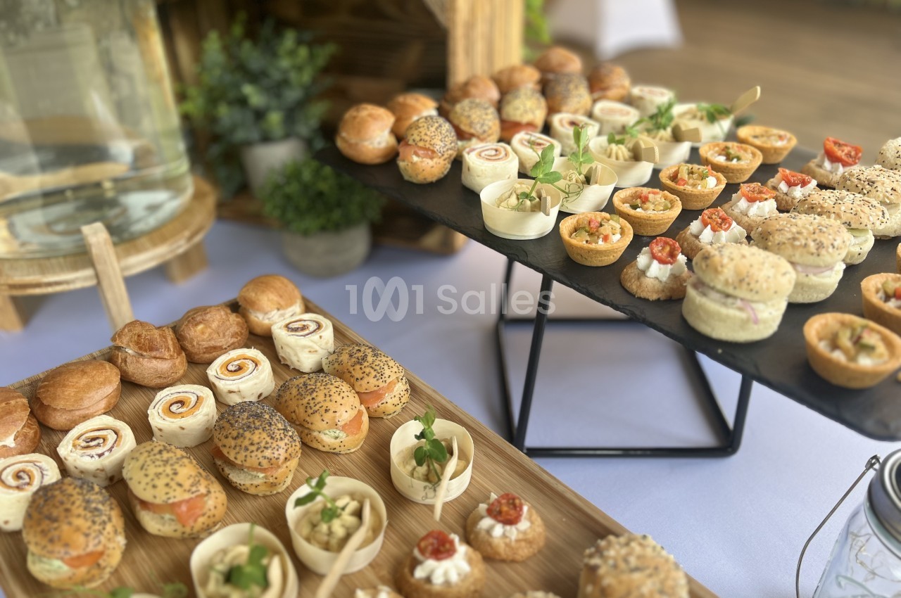 Plateaux de cocktail dînatoire : mini-sandwichs ronds garnis de saumon, roulés de tortilla, bouchées en coupelles et tartelettes garnies, sur planches en bois et ardoise.