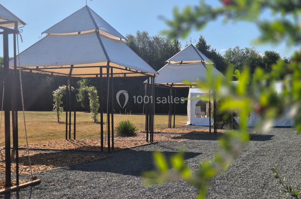Tentes blanches avec structures métalliques dans un espace extérieur ensoleillé, entouré de végétation et de gravier.