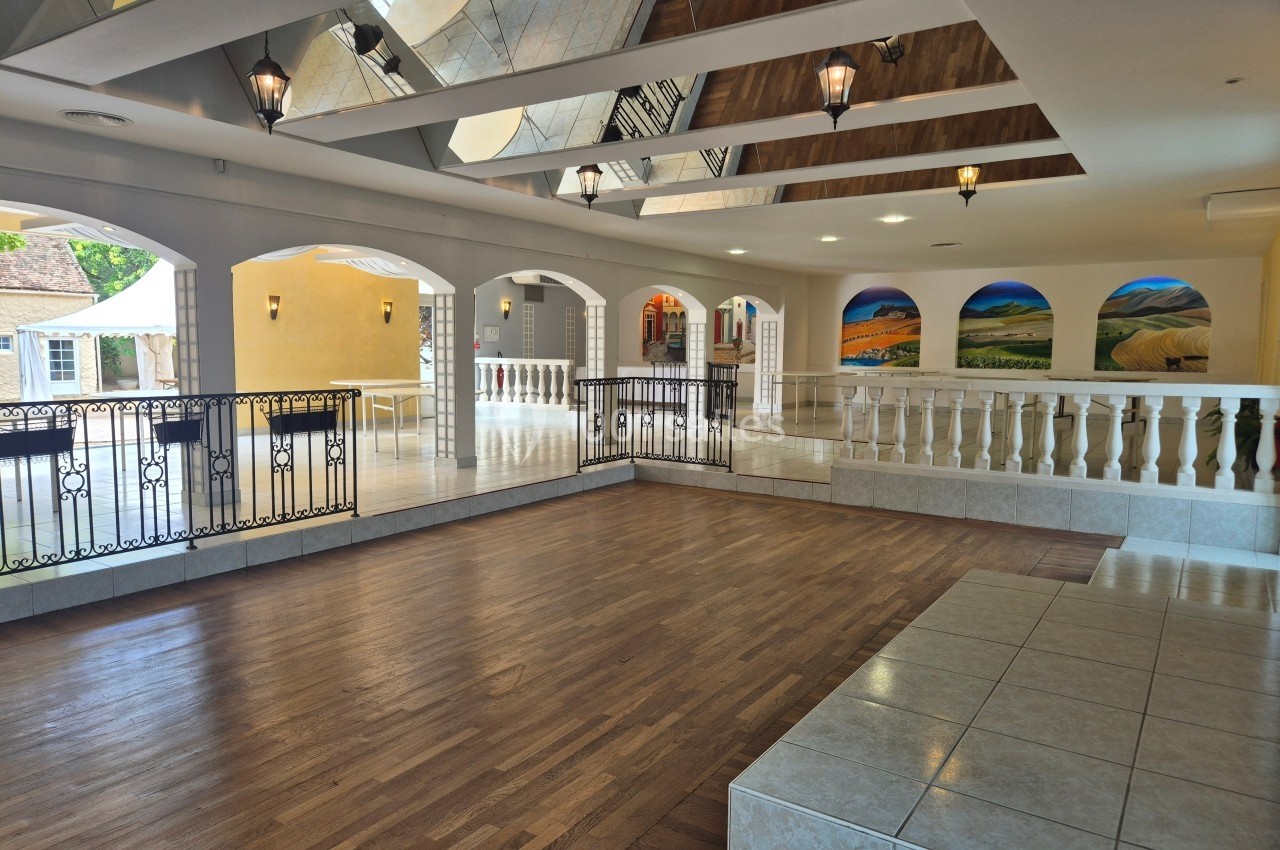 Salle spacieuse avec parquet, balustrades blanches, murs décorés de fresques paysagères et plafonds avec miroirs.