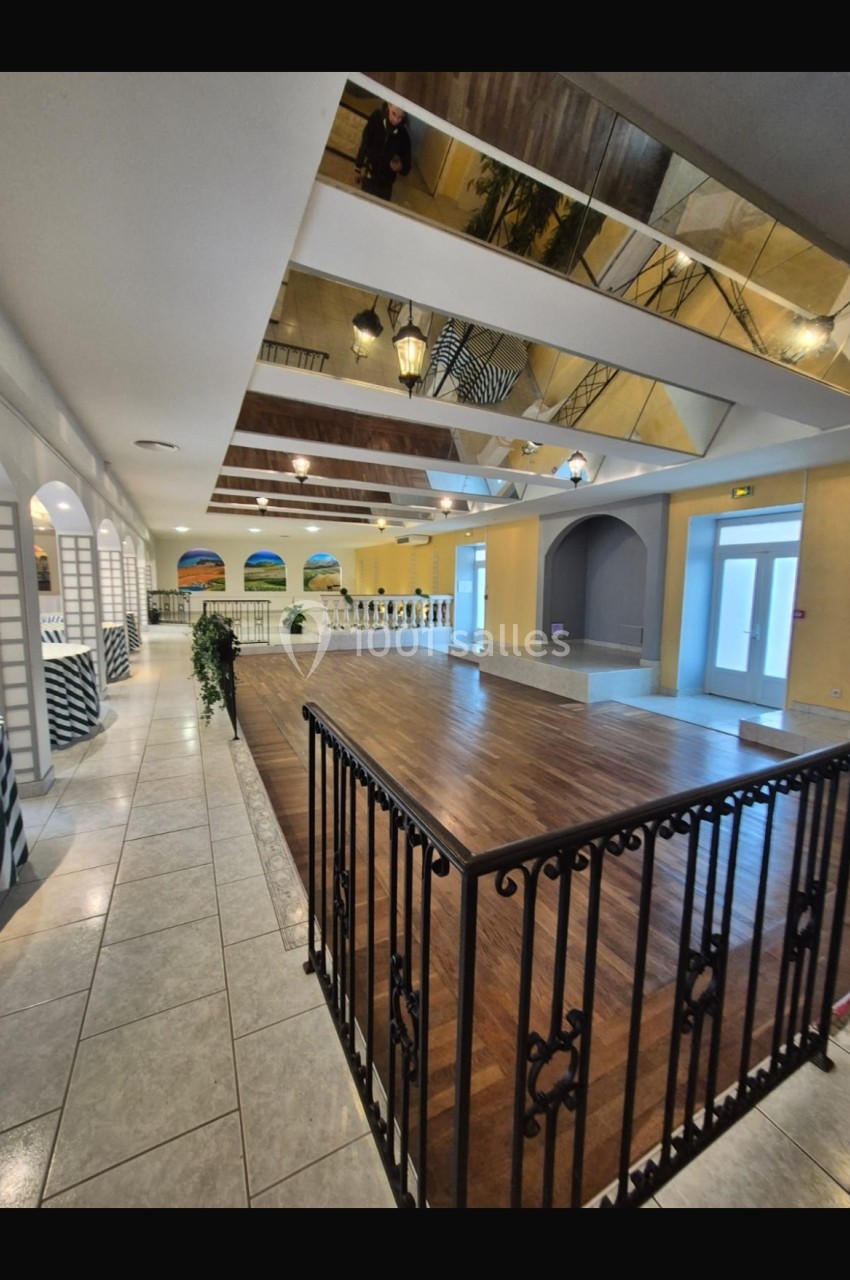 Salle spacieuse avec parquet, balustrade en fer forgé, plafond avec miroirs et éclairage suspendu.