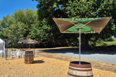 Miniature Location salle Souligné-sous-Ballon (Sarthe) - Le Grand Chêne #15 Deux tonneaux en bois avec parasols sur un sol gravillonné, près d'arbres sous un ciel bleu.