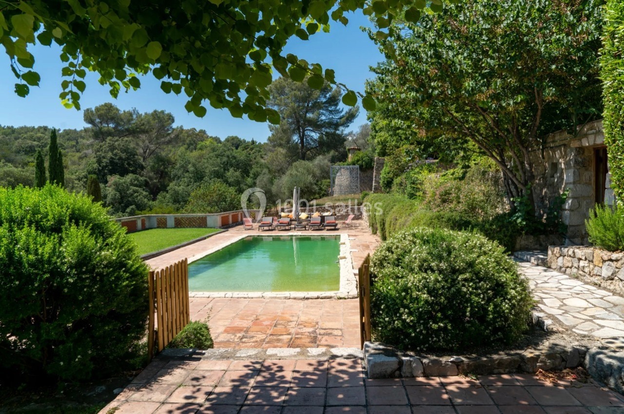 Piscine extérieure entourée de végétation, avec des chaises longues alignées sur une terrasse ensoleillée.