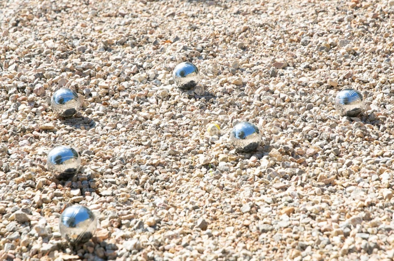 Boules de pétanque en métal et cochonnet jaune disposés sur un terrain de gravier.