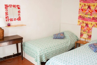 Chambre lumineuse avec lit double, couvre-lit bleu, lampe de chevet et porte-fenêtre donnant sur un jardin.