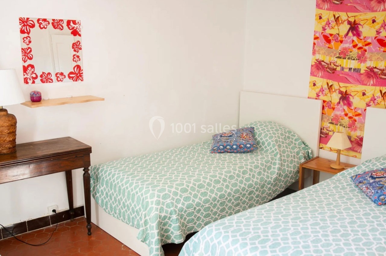 Deux lits simples avec couvre-lits verts dans une chambre lumineuse, décorée de motifs colorés et d'un bureau en bois.