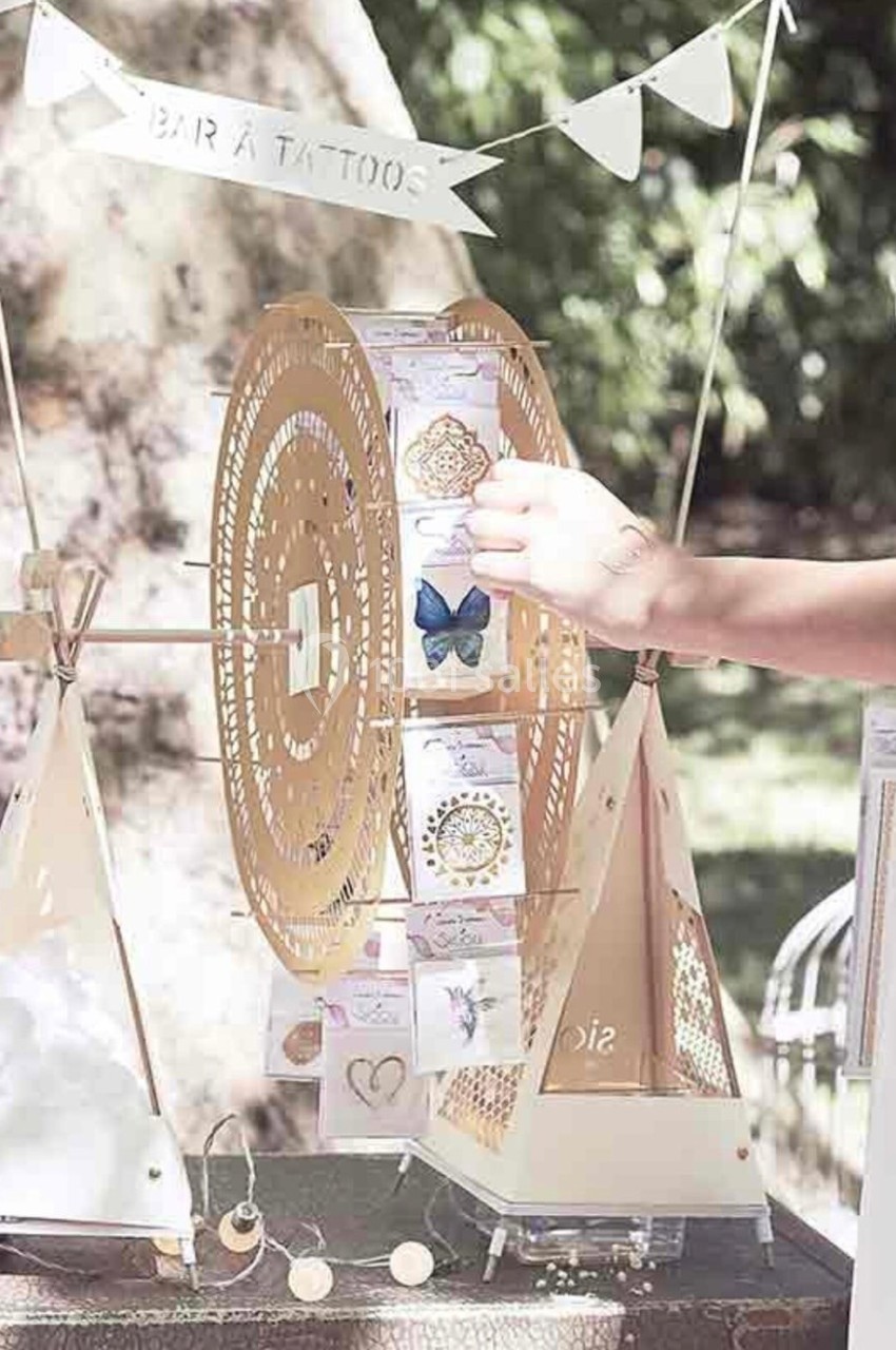 Femme sélectionnant un tatouage temporaire sur une roue dorée dans un stand en plein air décoré de façon festive.