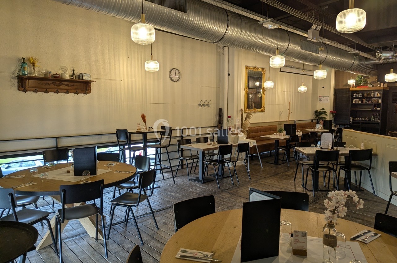 Salle de restaurant lumineuse avec tables en bois, chaises noires, décorations murales et éclairage suspendu.