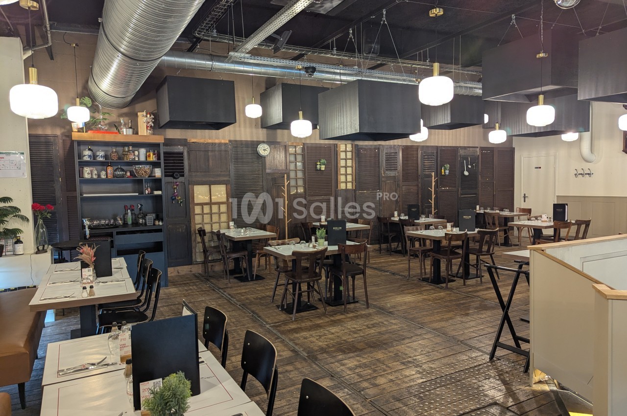Salle de restaurant moderne avec tables dressées, éclairage suspendu et décoration industrielle.