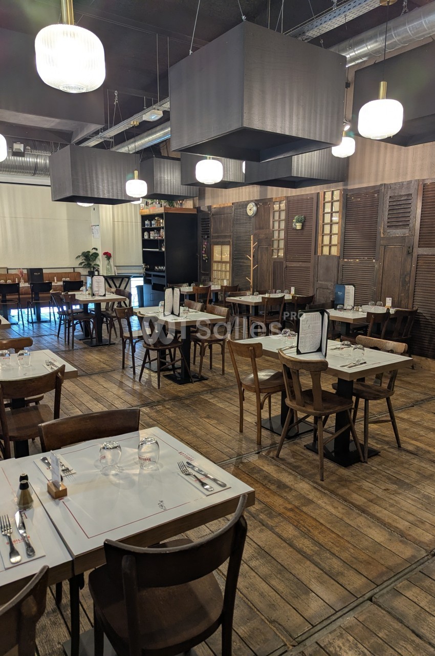 Salle de restaurant avec tables en bois dressées, éclairage suspendu et décor chaleureux en bois et métal.