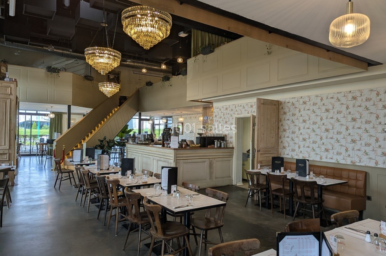 Salle de restaurant lumineuse avec tables dressées, chaises en bois, lustres suspendus et décoration intérieure élégante.