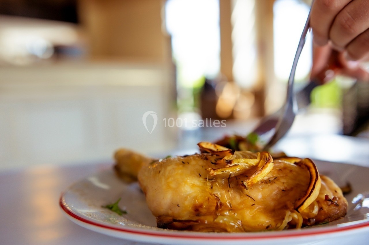 Poulet rôti garni d'oignons caramélisés sur une assiette, avec une main utilisant une fourchette en arrière-plan.
