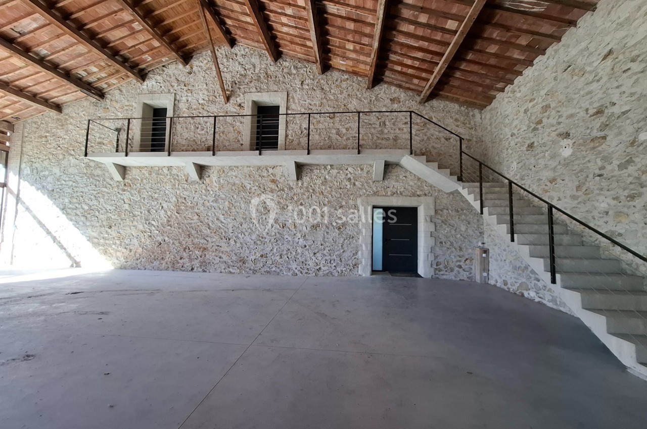 Intérieur d'un bâtiment en pierre avec mezzanine, escalier en béton et plafond en bois.