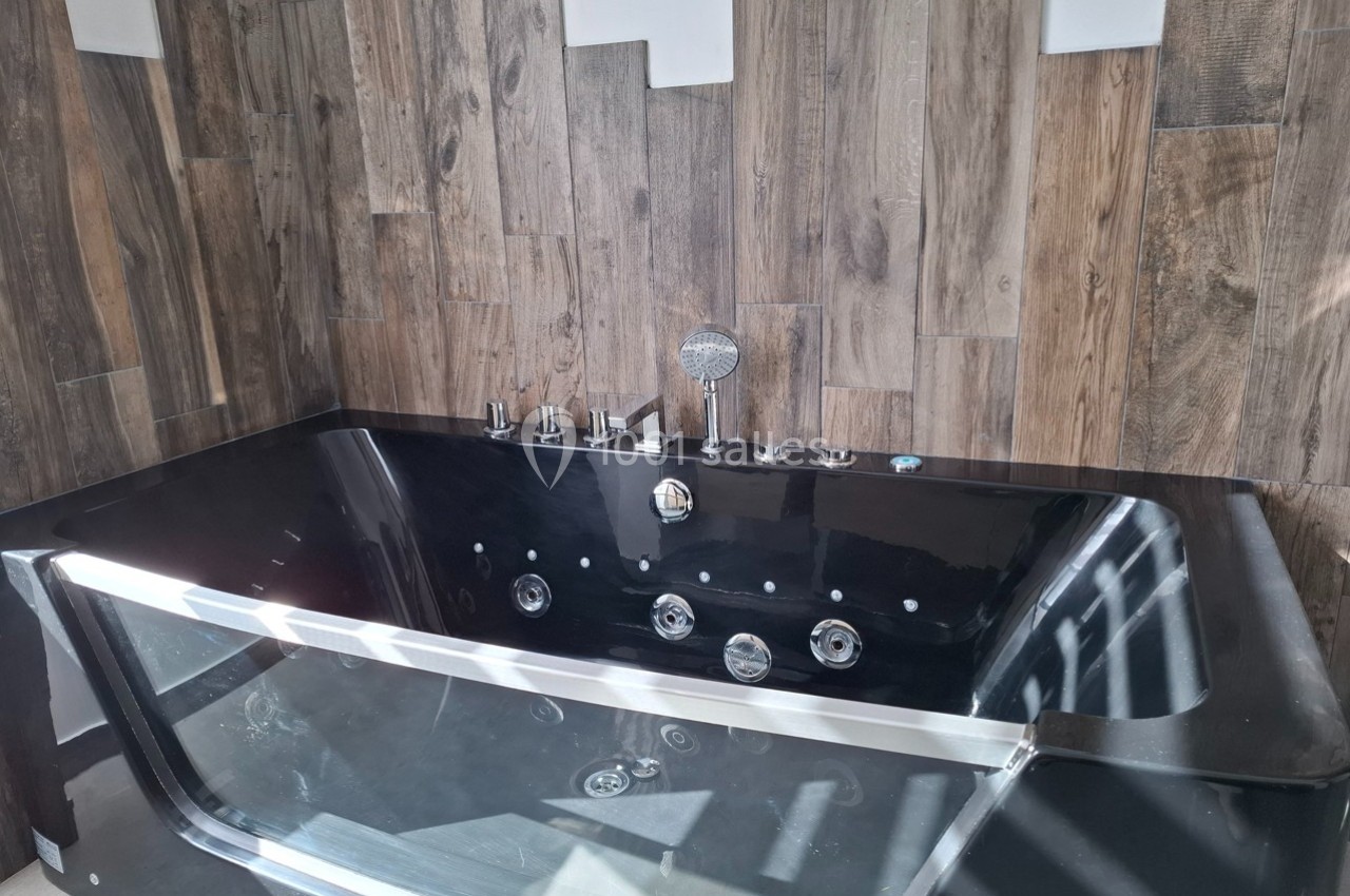 Baignoire noire moderne avec jets intégrés, installée devant un mur en bois aux teintes naturelles.