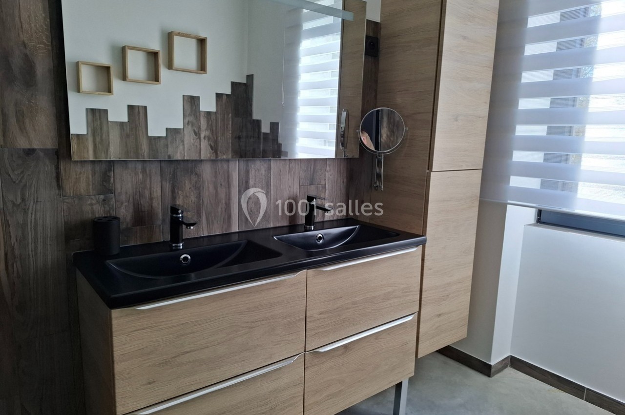 Double vasque moderne avec meubles en bois clair, miroir large, mur en bois et store enrouleur blanc à rayures.