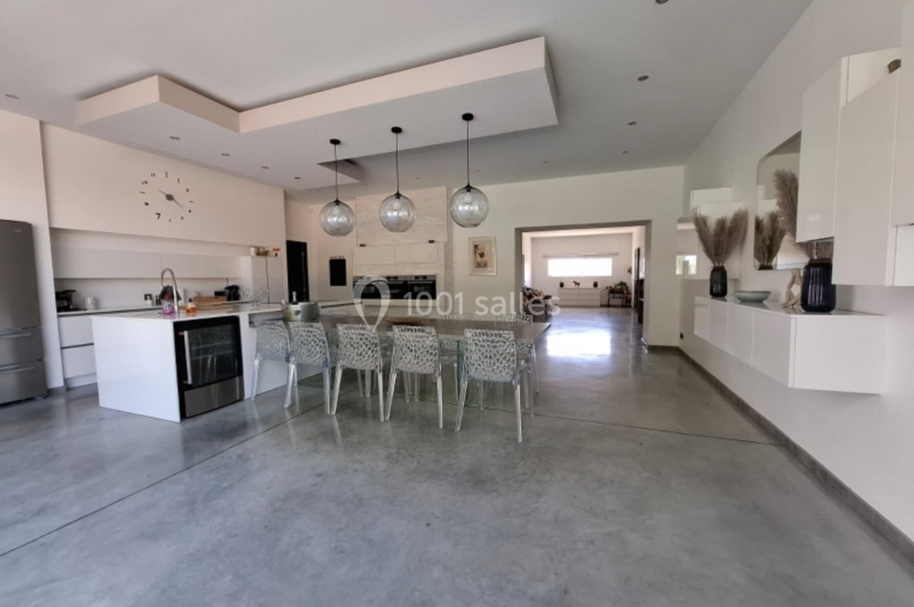 Cuisine moderne avec îlot central, table à manger, luminaires suspendus et sol en béton poli.