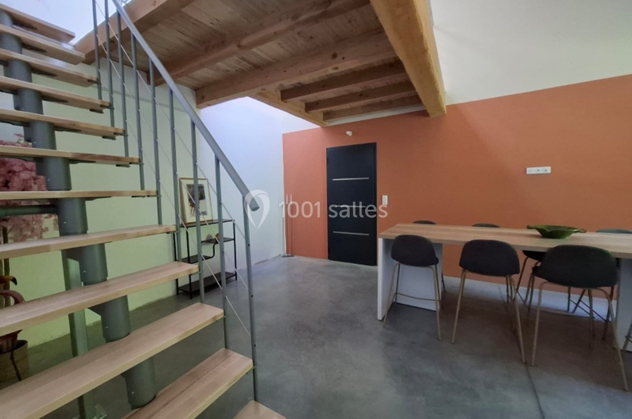 Escalier en bois et métal menant à une mezzanine, avec une table et des chaises dans un espace à mur orange.