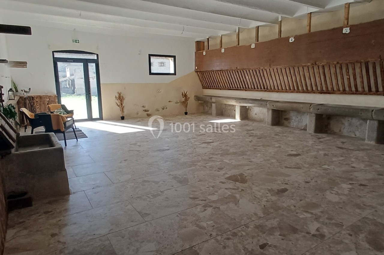 Salle vide avec sol en carrelage, murs clairs, bancs en pierre et rangées de râteliers en bois le long d'un mur.