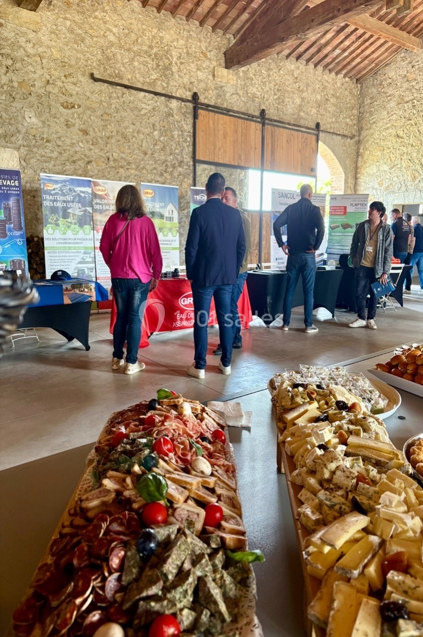 Plateau de charcuteries et fromages au premier plan, avec des stands d'exposition et des visiteurs en arrière-plan.