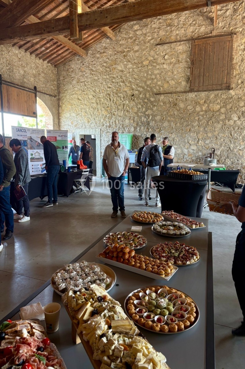 Buffet varié avec amuse-bouches, fromages et desserts dans une salle en pierre avec des stands en arrière-plan.