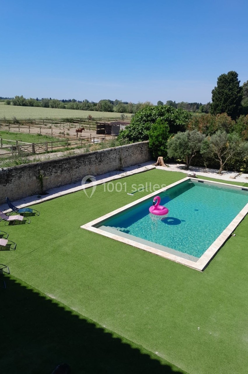 Piscine rectangulaire avec une bouée rose en forme de flamant rose, entourée de pelouse et d'une clôture en pierre.