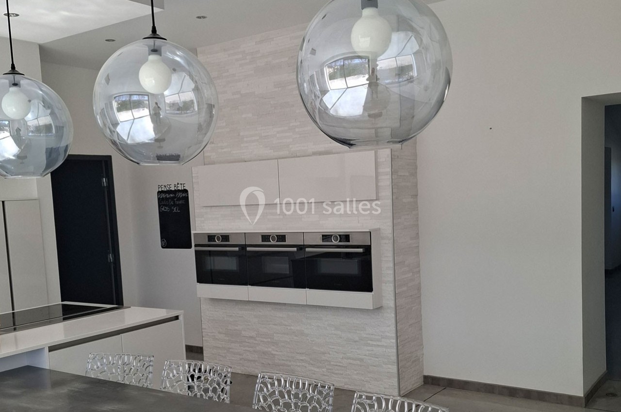 Cuisine moderne avec des fours encastrés, un îlot central, des suspensions sphériques et des chaises design.
