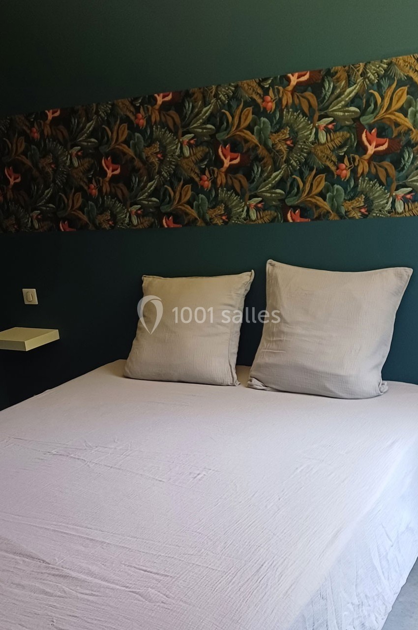 Lit double avec drap blanc, deux oreillers et tête de lit décorée d'un motif floral sur fond vert.
