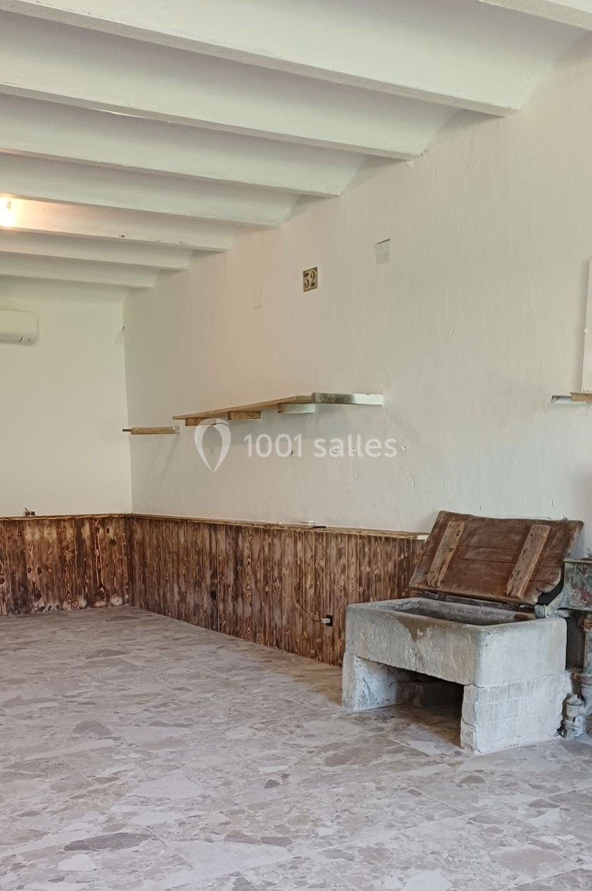 Une pièce vide avec murs blancs, étagères en bois, lambris bas et un ancien foyer en pierre.