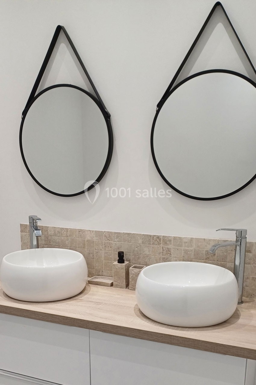 Deux vasques blanches sur un plan en bois clair, avec deux miroirs ronds suspendus au mur.