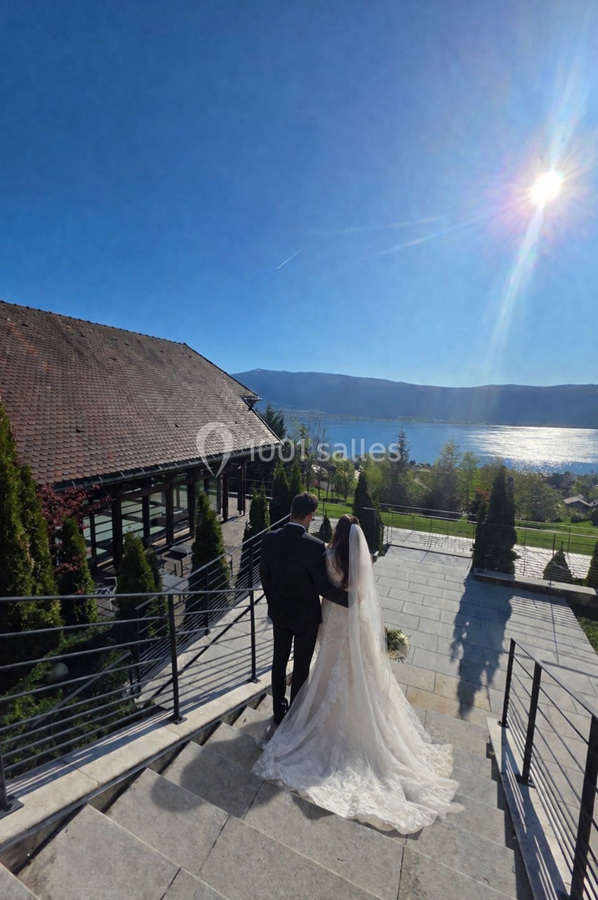 Un couple en tenue de mariage descend des escaliers extérieurs, avec vue sur un lac et un paysage ensoleillé.