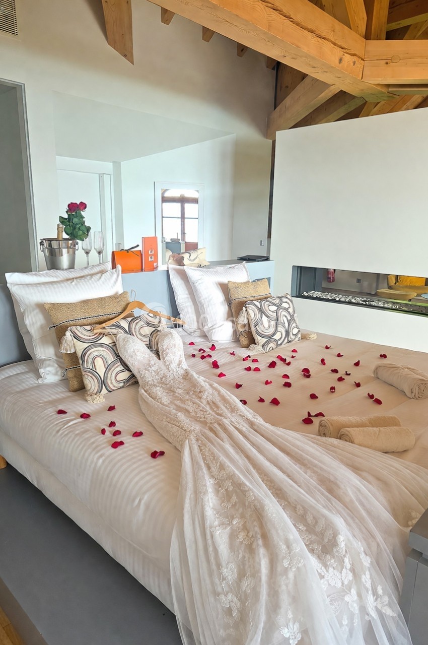 Lit décoré avec une robe de mariée, des pétales de rose, des serviettes pliées et un seau à champagne dans une chambre…