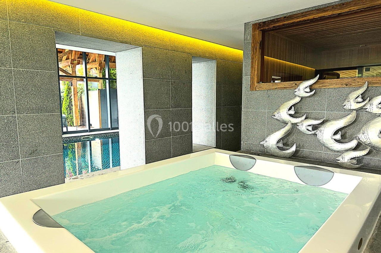 Bain à remous dans une pièce moderne avec murs en pierre grise, vue sur une piscine et sculptures murales décoratives.