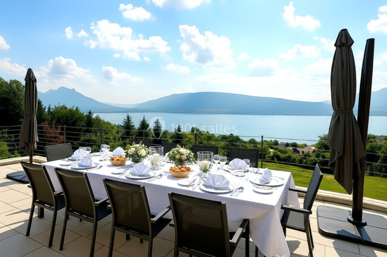 Table dressée en extérieur avec vue sur un lac et des montagnes, entourée de parasols fermés et de verdure.
