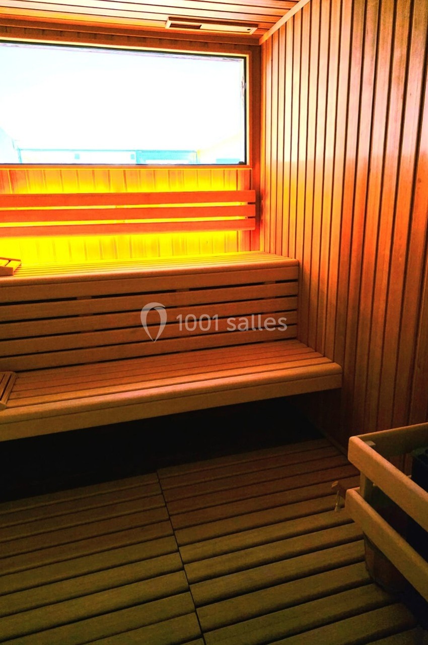 Intérieur d'un sauna en bois avec bancs superposés et lumière chaude provenant d'une fenêtre rectangulaire.