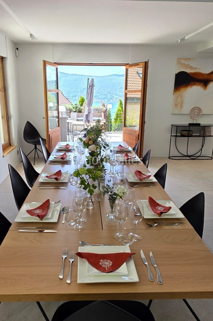Table dressée avec vaisselle, verres et serviettes rouges, dans une salle lumineuse avec vue sur une terrasse et des…