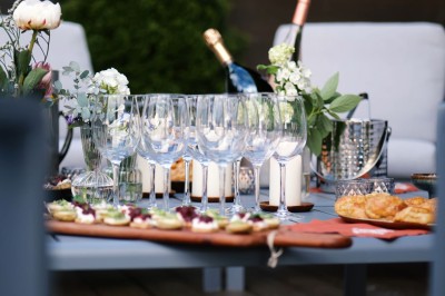 Table extérieure dressée avec des verres à vin, des fleurs, des bougies et des plateaux de nourriture.