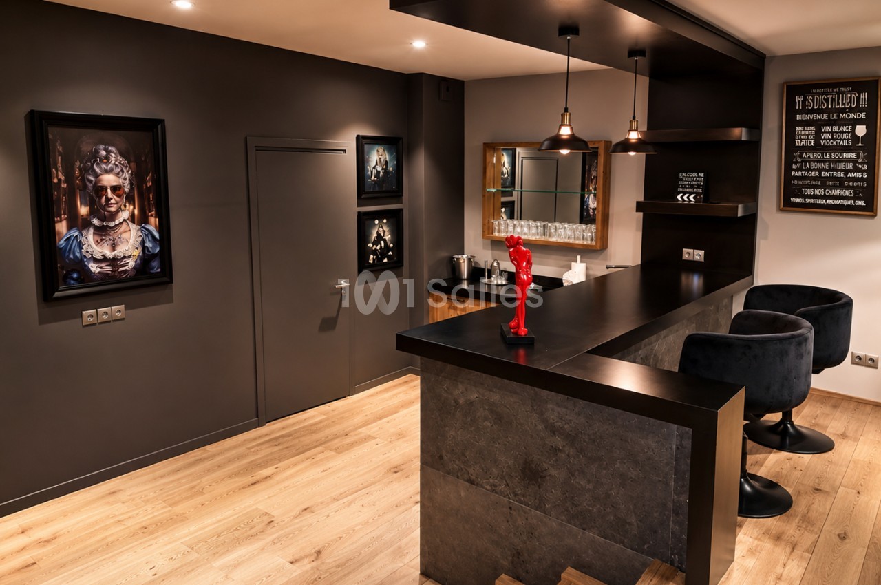 Salle de dégustation intérieure avec comptoir noir, tabourets, sol bois et murs gris anthracite.