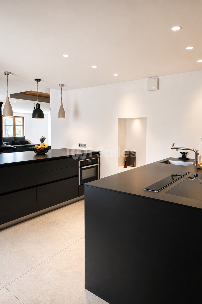 Cuisine ouverte avec îlot et plan de travail gris, meubles noirs, éclairage encastré au plafond blanc.