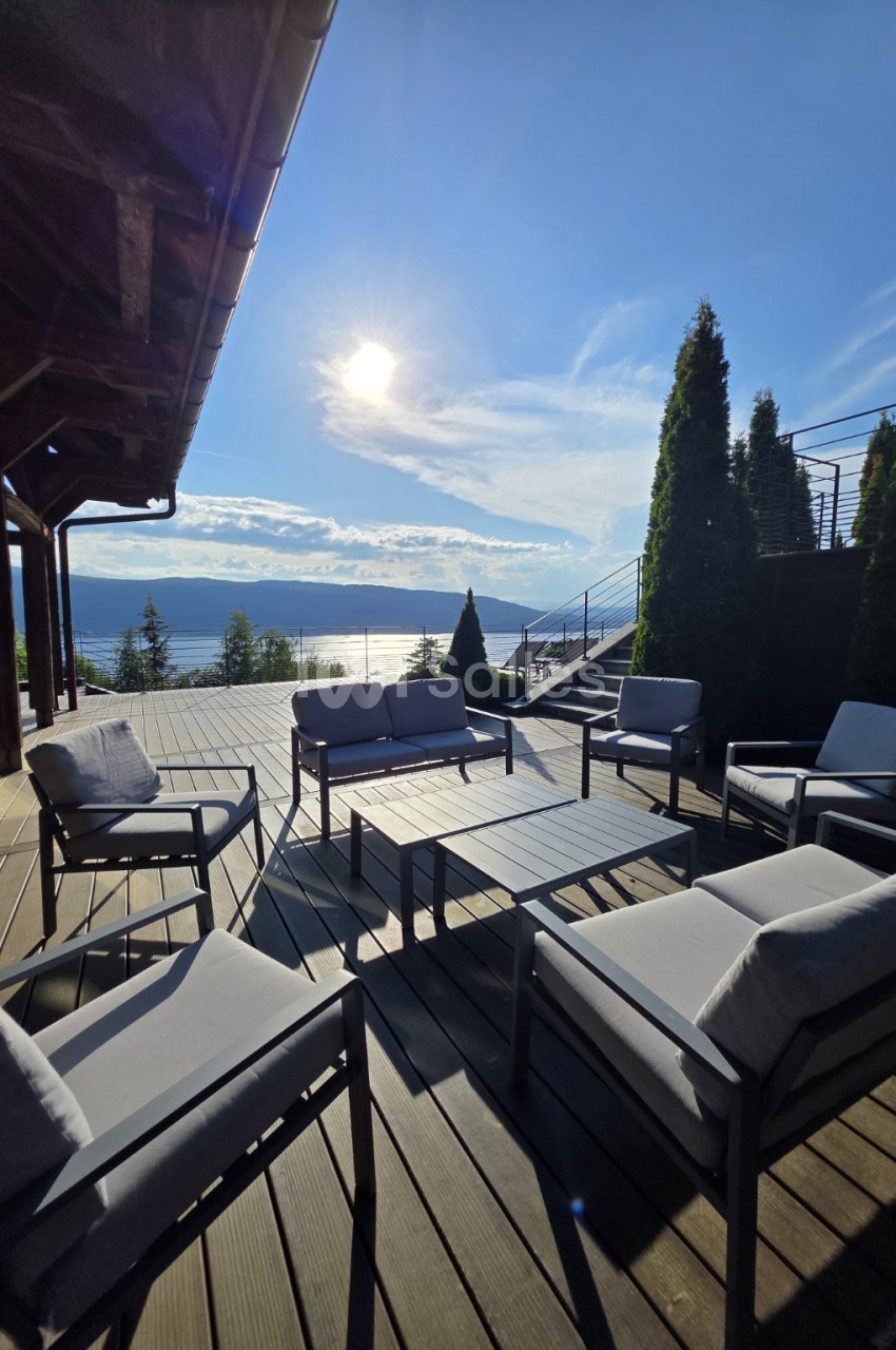 Terrasse couverte avec mobilier de détente face au lac d'Annecy et aux montagnes enneigées.