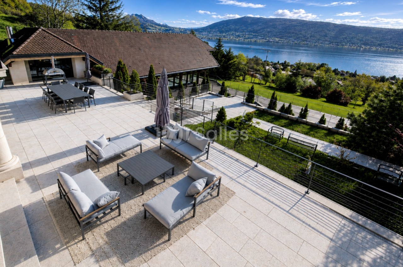 Terrasse panoramique avec salon de jardin, parasol, lac et montagnes en arrière-plan.