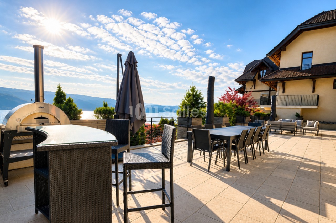 Terrasse avec tables dressées, parasols fermés, four à pizza et villa sur lac de montagne par temps clair.