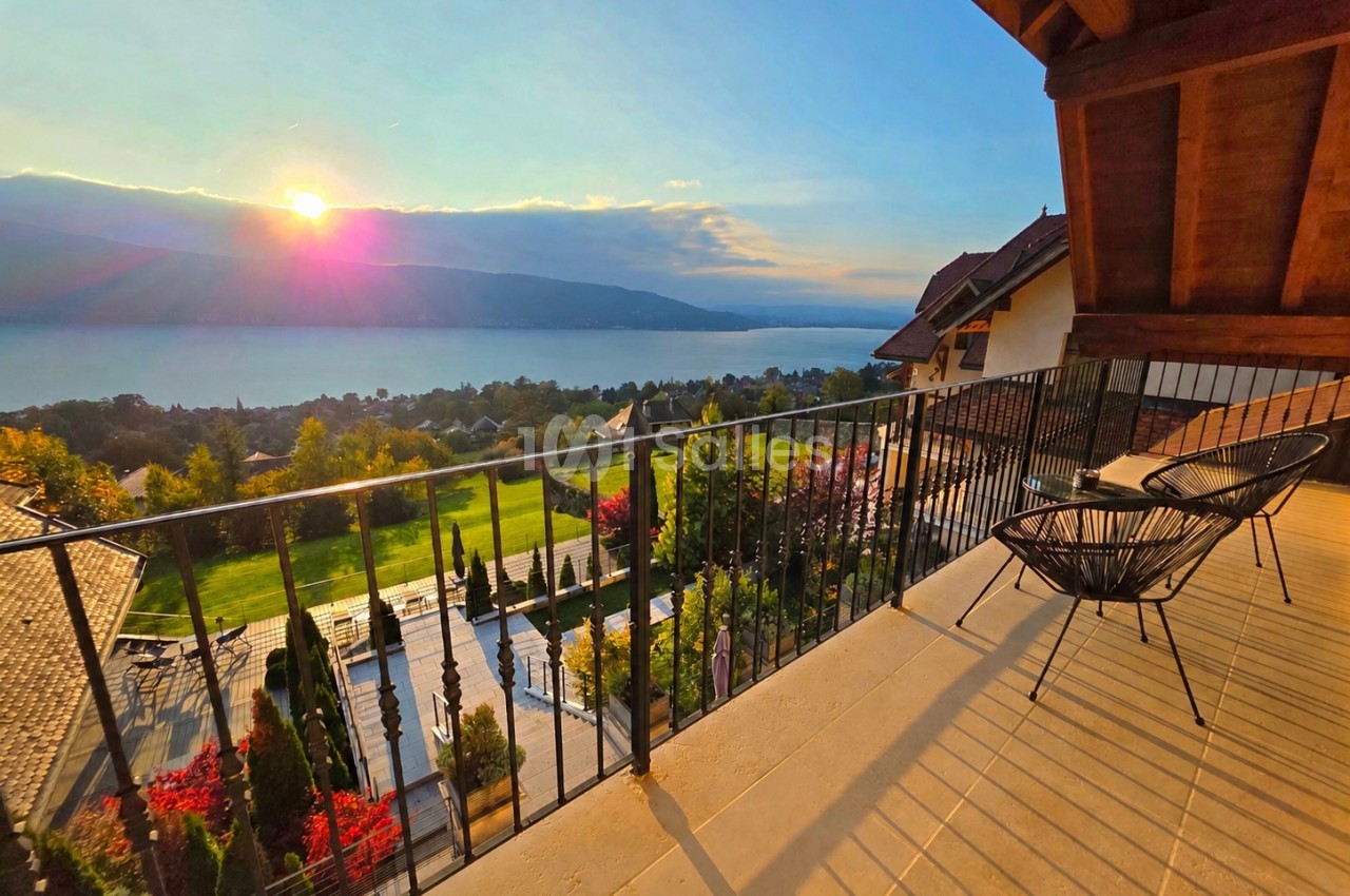 Terrasse avec chaises face au lac Annecy au coucher de soleil, montagnes en arrière-plan.