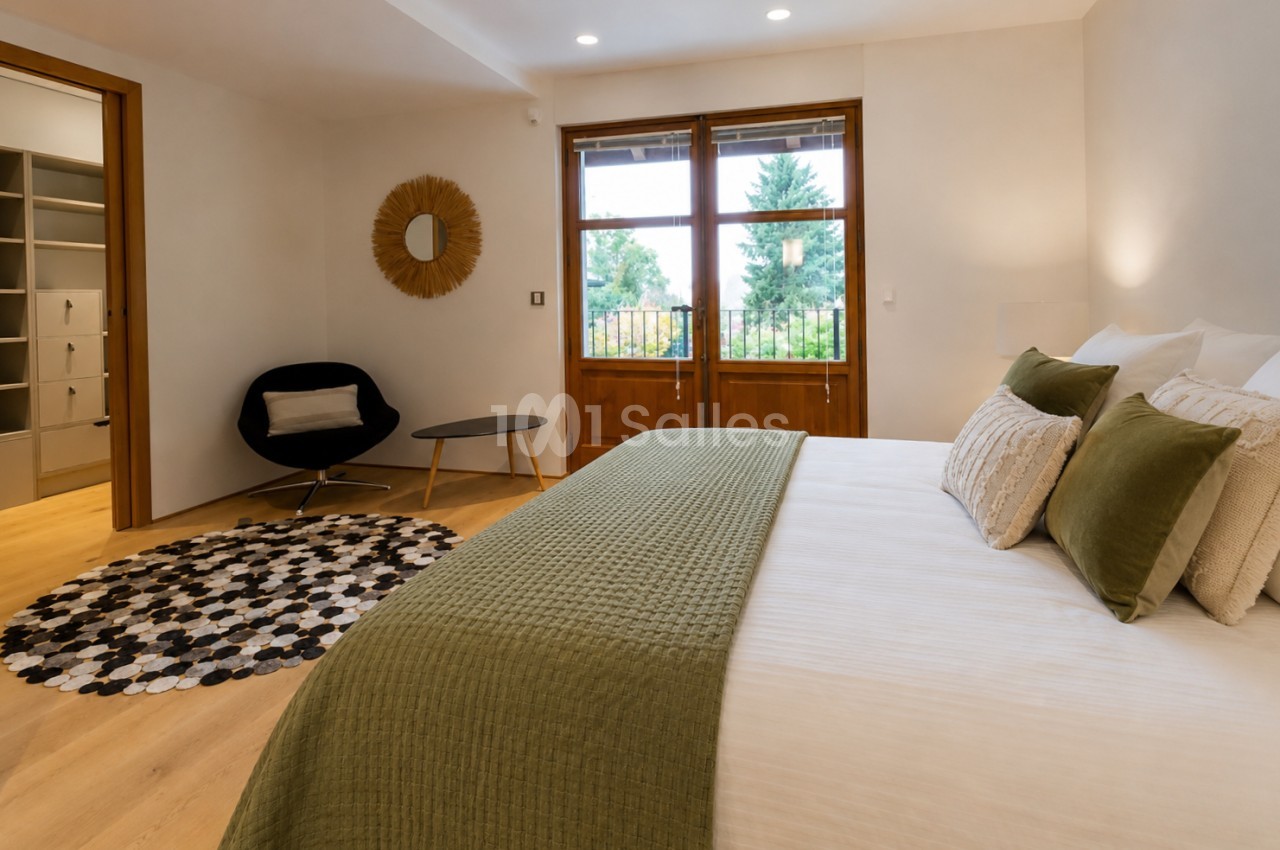 Chambre avec lit double aux draps verts, baies vitrées ouvrant sur jardin et montagnes.